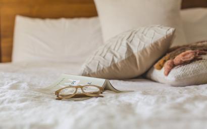 bril ligt op een boek op een bed met witte kussens