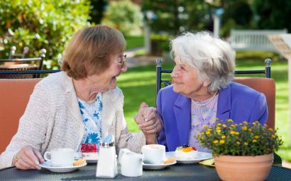 twee oudere dames kletsen geellig over koffie in de tuin