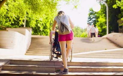 Jonge vrouw die een persoon in een rolstoel een trap op helpt