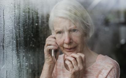 Foto van oudere vrouw achter een raam die aan het bellen is