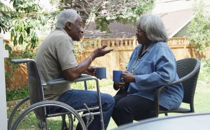 Oudere zwarte man zit in een rolstoel en praat met een oudere vrouw