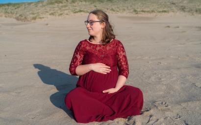 Foto van Sharon die zwanger is. Ze zit op het strand en draagt een rode jurk.