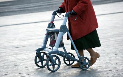oudere vrouw loopt met rollator over straat