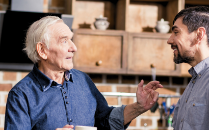 Foto van een oudere man en een jongere man die staan te praten