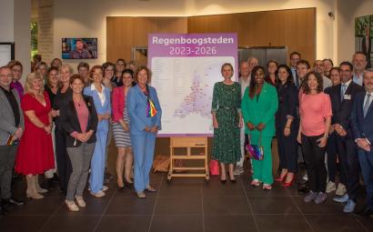 Foto van wethouders rondom een bord waarop een kaart van Nederland staat waarop te zien is welke gemeenten Regenbooggemeenten zijn