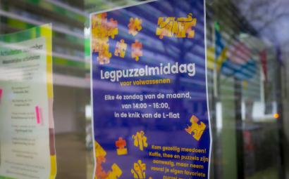 Foto van een poster met een advertentie voor een legpuzzelmiddag door een raam heen genomen.