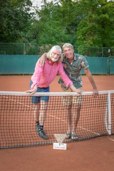 Ed en Tom staan naast elkaar op de tennisbaan achter het net