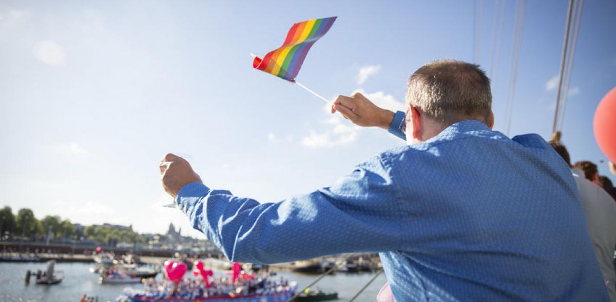 Man met regenboogvlag zwaait naar boot tijdens canal parade