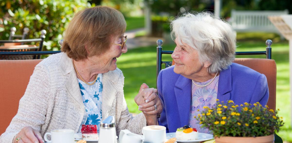 twee oudere dames kletsen geellig over koffie in de tuin