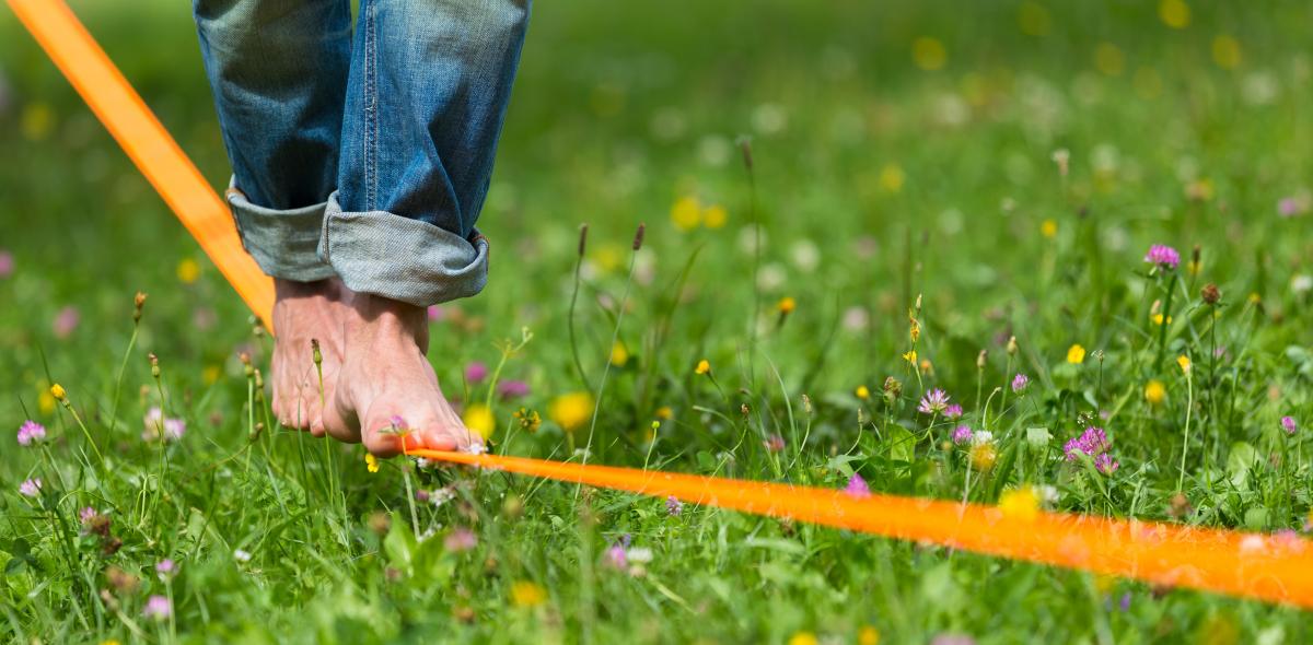 Foto van voeten balancerend op de oranje band, vlak boven een grasveld