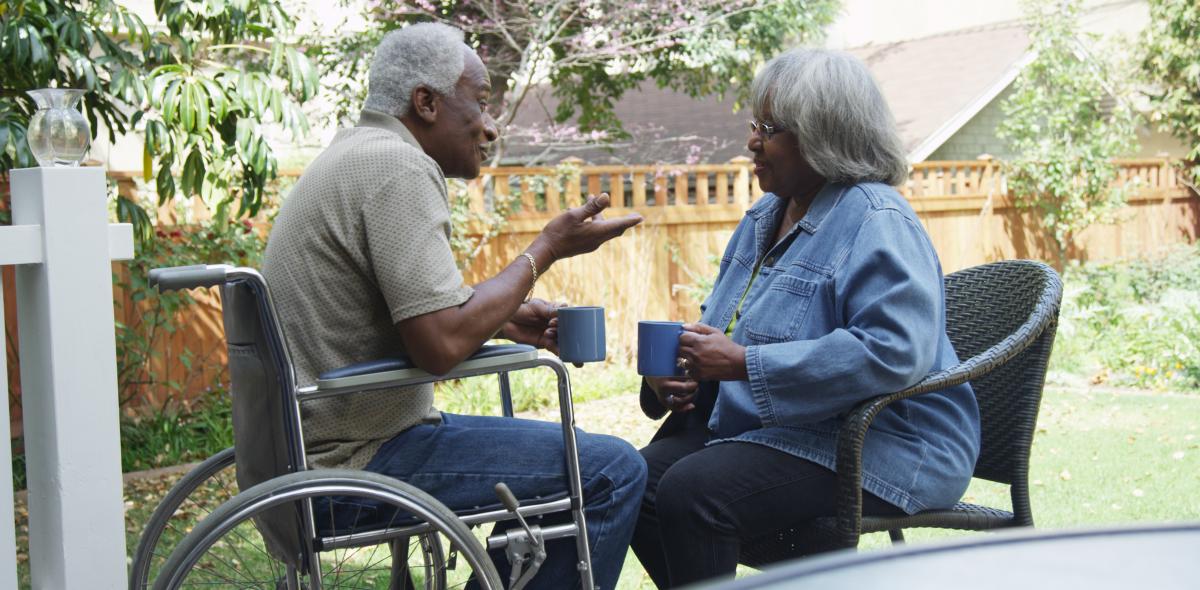 Oudere zwarte man zit in een rolstoel en praat met een oudere vrouw