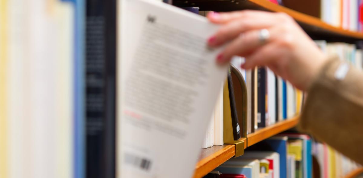 Een hand pakt een boek uit een boekenkast.